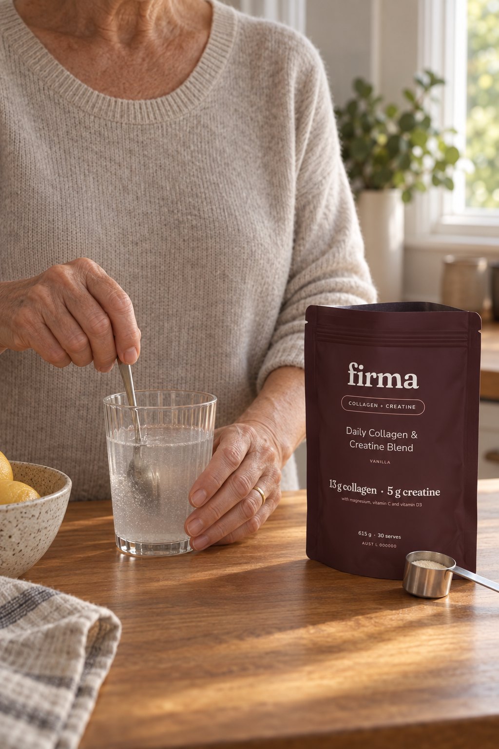 Hands of a woman in her late sixties stirring a glass of water at a timber kitchen bench beside an open oxblood firma pouch